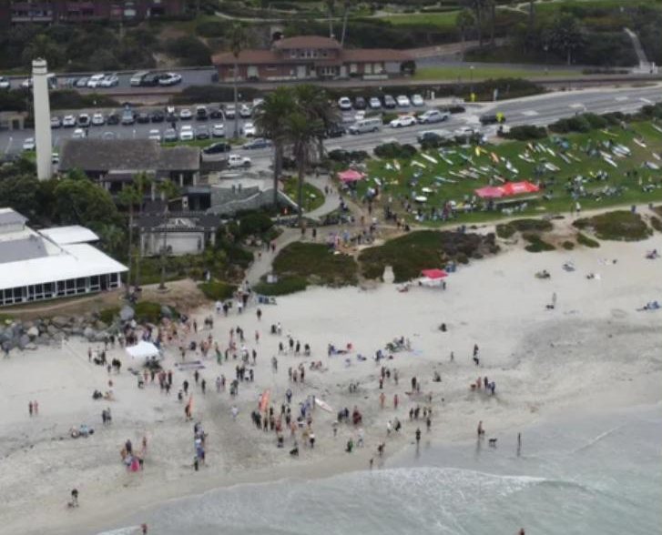Aerial view of Del Mar's Powerhouse Park and beach with event tents and paddleboards laid out on the grass.